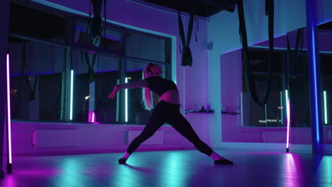 A-woman-dances-in-a-studio-with-a-neon-light-performing-graceful-exercises-and-movements-from-stretching-and-dancing-in-slow-motion